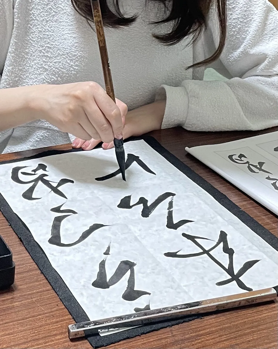 筆を運ぶ生徒の手元と、書きかけの作品